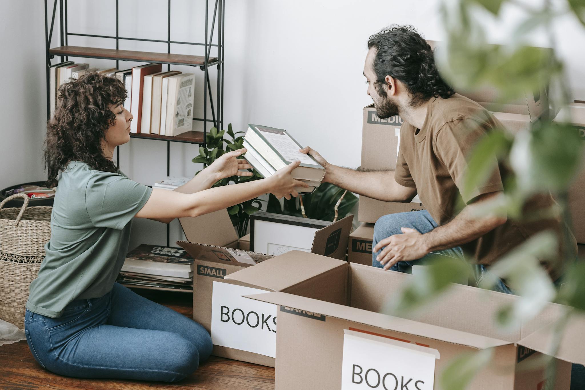 A couple organizing and packing books in cardboard boxes indoors, preparing for a move.